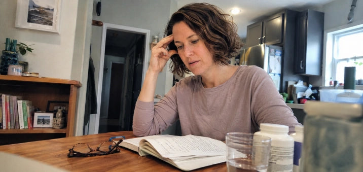 A woman at her kitchen table with a notebook and supplement bottles